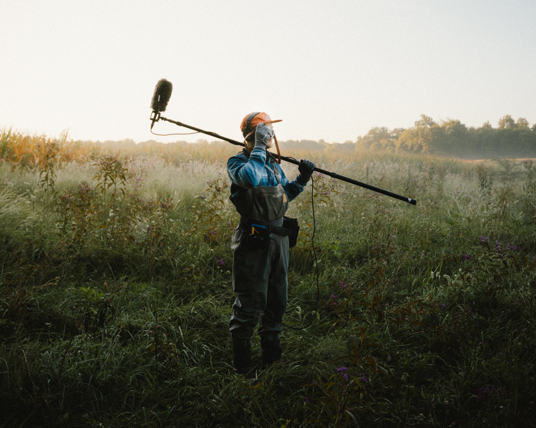 Sound recordist with boom microphone in a misty meadow at dawn