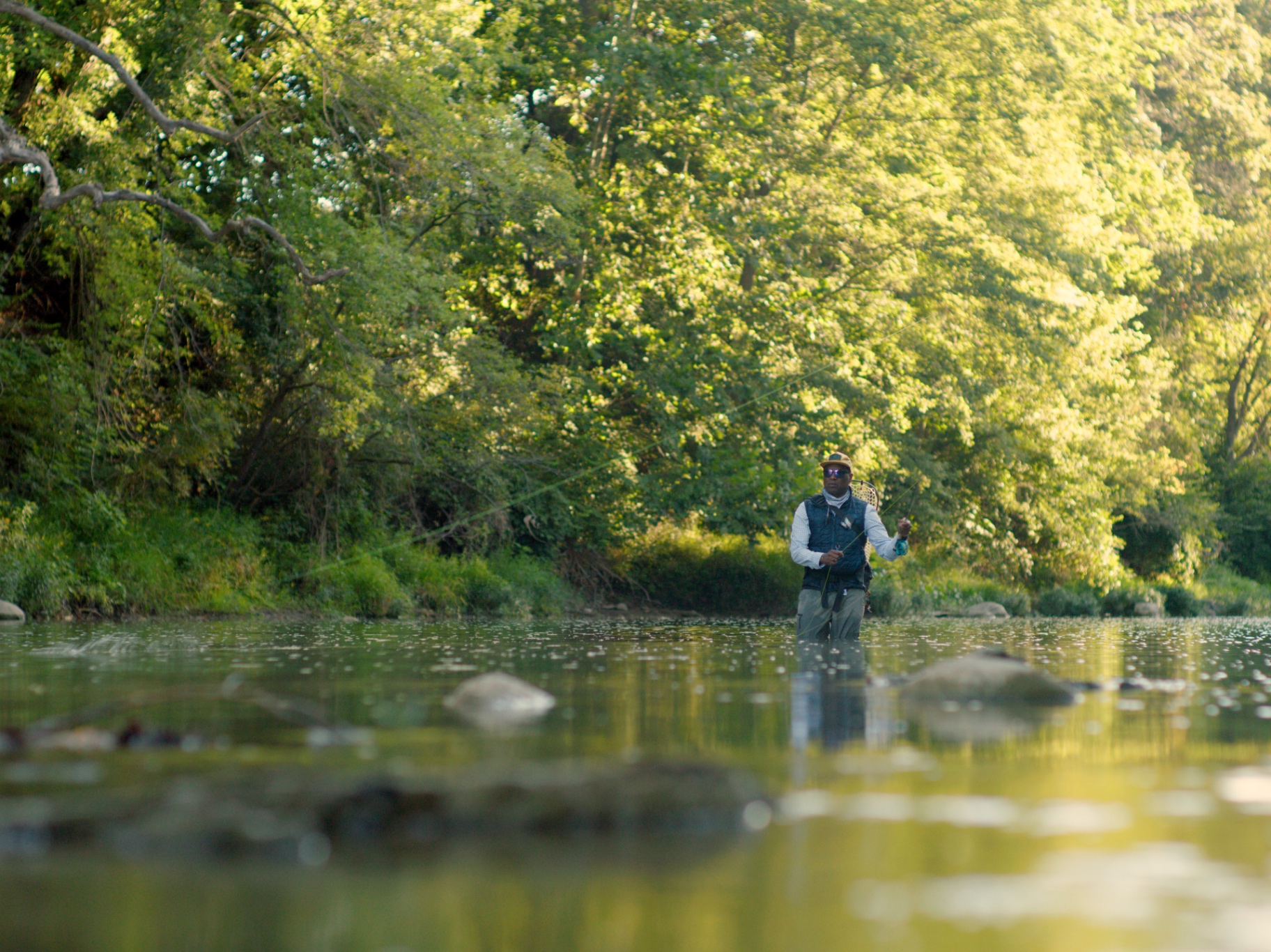Al wading into a wide Indiana stream surrounded by summer trees